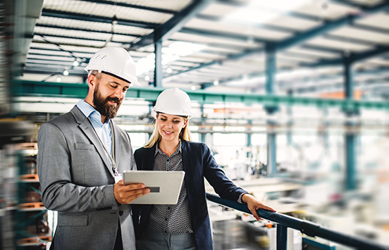 Two engineers in hard hats reviewing a tablet
